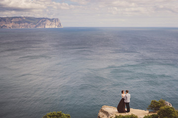 Romantic and stylish caucasian couple standing on the background of spectacular sea view. Love, relationships, romance, happiness concept.