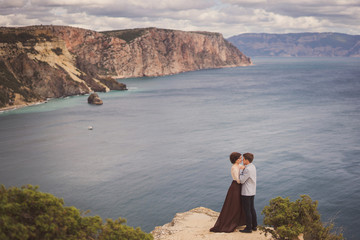 Romantic and stylish caucasian couple standing on the background of spectacular sea view. Love, relationships, romance, happiness concept.