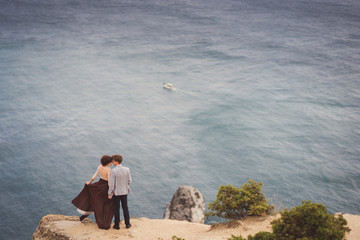 Romantic and stylish caucasian couple standing on the background of spectacular sea view. Love, relationships, romance, happiness concept.