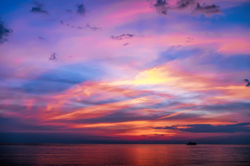Tropical colorful dramatic sunset with cloudy sky and silhouette of the ship on the horizon. Evening calm on the Gulf of Thailand. Bright afterglow.