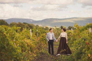 Romantic and stylish caucasian couple standing in the beautiful vineyard at sunset. Love,...