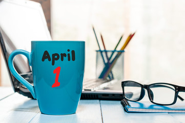 April 1st. Day 1 of month, calendar on morning coffee cup, business office background, workplace with laptop and glasses. Spring time, empty space for text