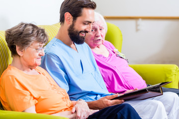 Altenpfleger schaut Fotos mit Senioren im Altenheim an