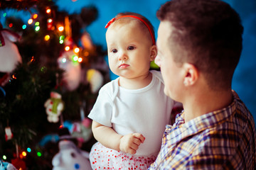 Girl in white shirt held by her father before a Christmas tree