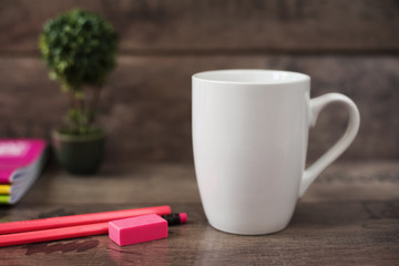 White mug mockup. Blank mug. Coffee mug mockup with bright neon colors pencils and notebooks. Potted plant bonsai behind. Rustic wooden background.