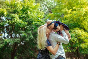 Dreamy mother kisses a girl with spiotted bow while dad holds he