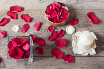 Glass vase and wood bow filled with red rose petals, white aromatic vanilla candle. Wooden background. Aromatherapy concept. Romantic background