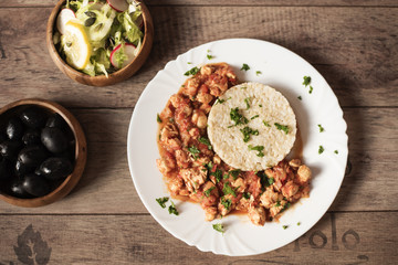 Chicken with rice, olives and green iceberg lettuce salad with cucumbers. Rustic wooden background.