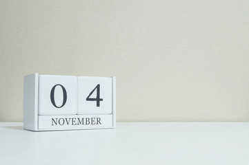 Closeup white wooden calendar with black 4 november word on blurred white wood desk and cream color wallpaper in room textured background with copy space , selective focus at the calendar