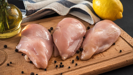 Raw chicken breasts and spices on wooden cutting board