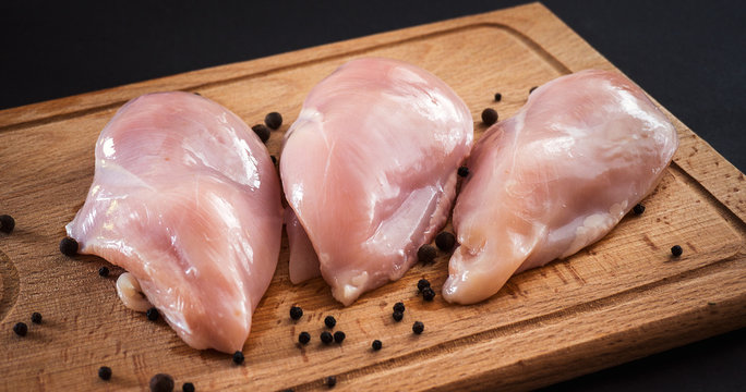 Raw chicken breasts and spices on wooden cutting board