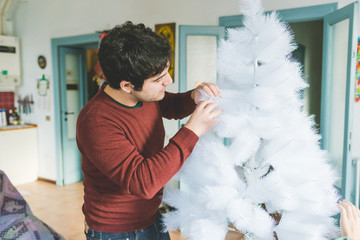 young handsome caucasian man assembling christmas tree, looking downward, concentrate - christmas, holiday, winter concept