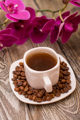 Small white cup of coffee, roasted coffee beans, orchid on wooden background