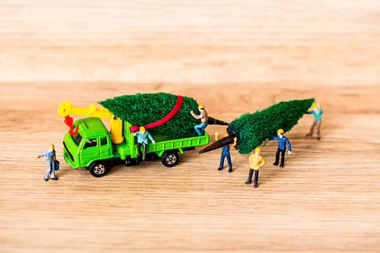 Miniature Worker Passenger Christmas Tree by Truck on Wooden floor ,Determined Image for Christmas Holiday and Happy New Year Gift Celebration concept.