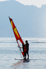 Unrecognizable man windsurfing at the sunset.