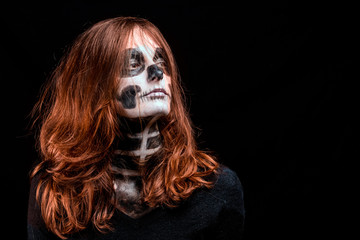 Une femme aux cheveux roux vifs et maquillée en squelette pose sur fond noir