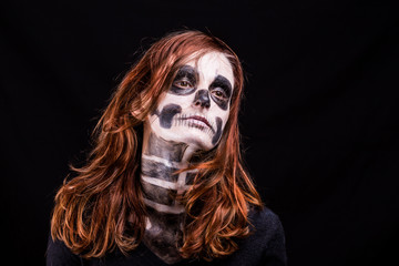 Une femme à la chevelure rousse vif et maquillée en squelette pose sur fond noir