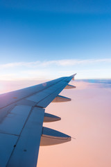 Fototapeta premium Wing of the airplane on blue and pink sky background at sunset