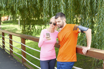 Obraz premium Fit couple after running. Full length shot of a young couple checking runner app on handy after morning workout.