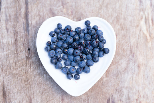 Fresh forest blueberries in heart plate on wooden background autumn