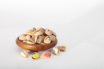 Roasted pistachio seeds with shell in wooden bowl on white background with copy space