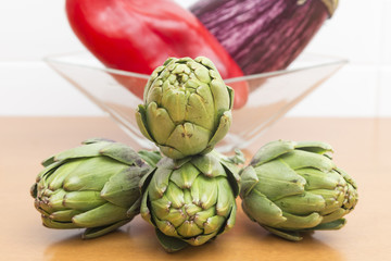 four artichokes in a dynamic assembly and a bowl with red vegeta