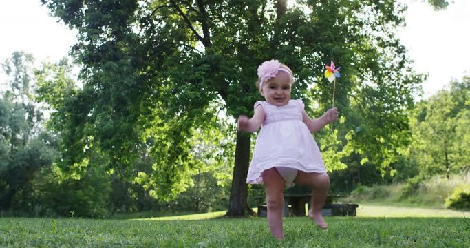 On a sunny day a baby takes its first steps on its own and in the hands of the newborn is a pinwheel, smiling and happy baby falls but rises again.