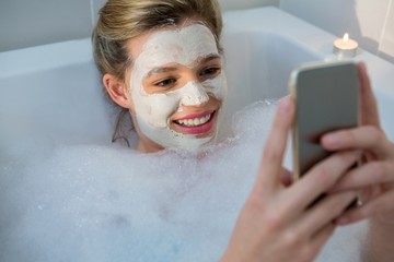 Woman using mobile phone while having bath in bathtub