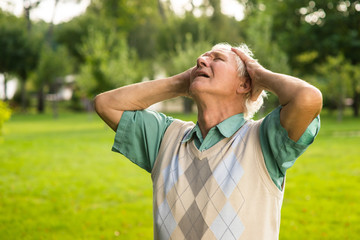 Man holding his head. Senior male on nature background. Grief and pain. I lost everything I loved.