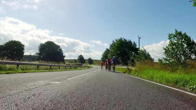 A stabilised view of a group of cyclists out on a training ride on country roads in the UK countryside on a sunny day. 