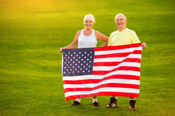 Senior couple holding US flag. Smiling man and woman outdoor. Patriots of strong country. Former...