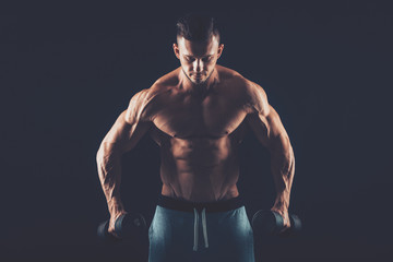 Fototapeta na wymiar Closeup of a muscular young man lifting dumbbells weights on dar