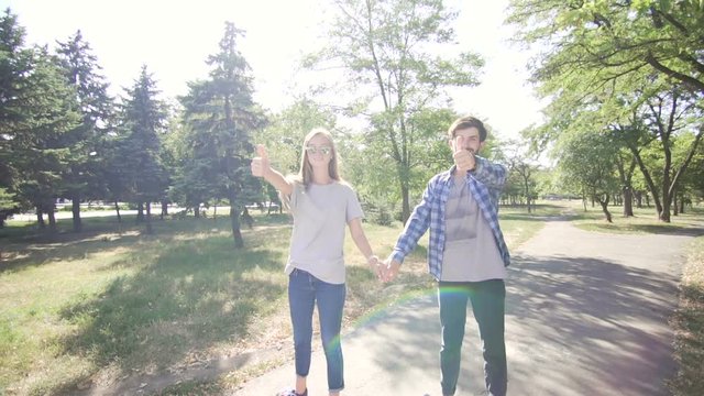 Young couple ridding hoverboard with holding hands and thumbs up. Wide shot