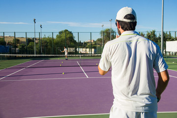 Professional tennis player playing the game on the tennis court. He has his back to the camera and have the racket in his right hand. 