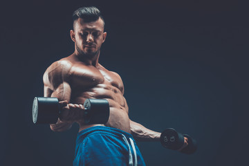 Closeup of a muscular young man lifting dumbbells weights on dar