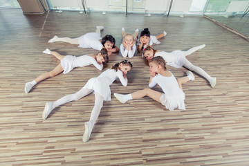 group of seven little ballerinas sitting on the floor. They are 