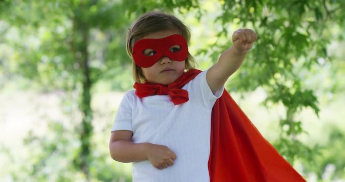 in a beautiful and happy sunny day , a little girl dressed as a super hero makes expressions and try to fly in the colorful nature , the child laughs happy . concept of happiness , love and nature.