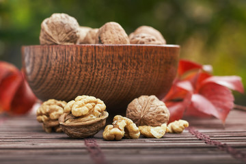 Walnuts in wooden bowl, green blurry background.