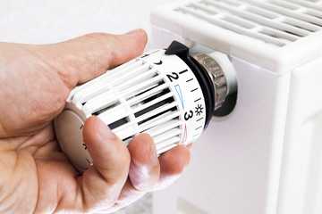 Hand is adjusting temperature of radiator. Low (cold) temperature setting. - 124916445