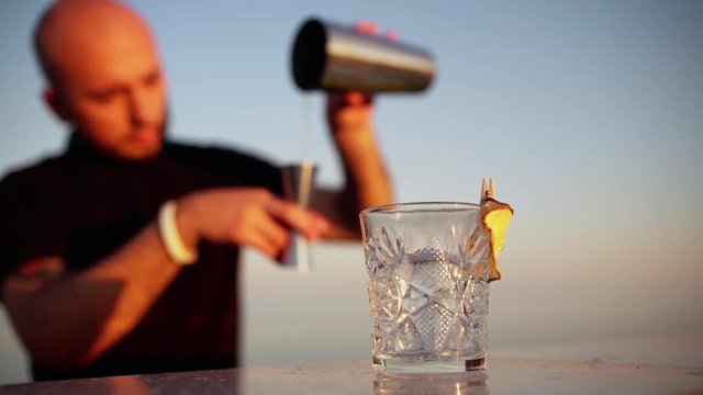 Young professional bartender preparing cocktail at seaside Slomo Focus on glass