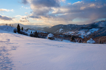 Fototapeta na wymiar Snow-covered haystacks on a snowy hillside at sunset. Winter mountain landscape.