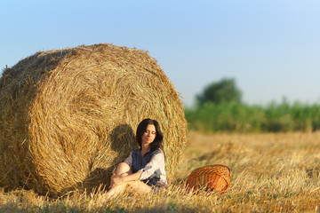 Naklejka na ściany i meble Girl with basket sitting in a field of straw