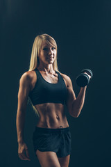 Athletic woman with dumbbells on a dark background