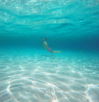 Man with glasses diving in a blue clean water of the sea