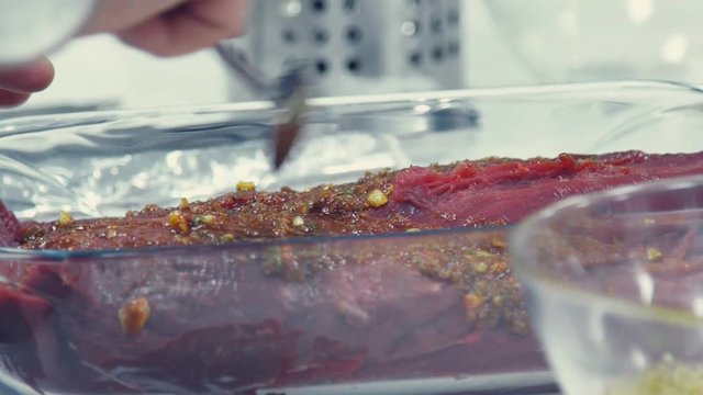 Slow motion: Raw meat in transparent refractory dish marinated in spices. Cooking a meat. High-calorie food. Food for men. Beef. Fresh and raw veal meat. Steaks with seasonings in a row ready to cook