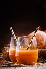 Pumpkin smoothie in glasses with tubes, vintage wooden backgroun