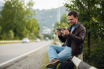 Obraz premium Man sitting on a road fence with gps tablet pc and using online maps
