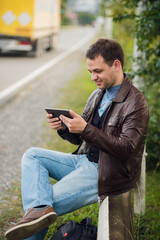 Obraz premium Man orders taxi from his tablet sitting on a road fence