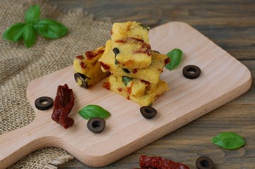 Gluten free meal from roasted corn flour, dried tomato, black olives and basil on wood on gunny cloth on brown wooden background