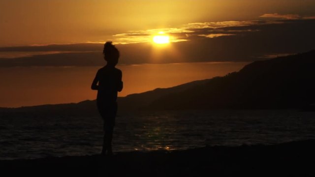 Silhouette, young girl walks on beach during sunset, Santa Monica, California.